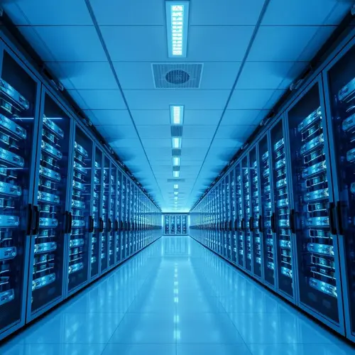 A wide-angle photograph of a modern data center with rows of server racks illuminated by cool blue and white lights.